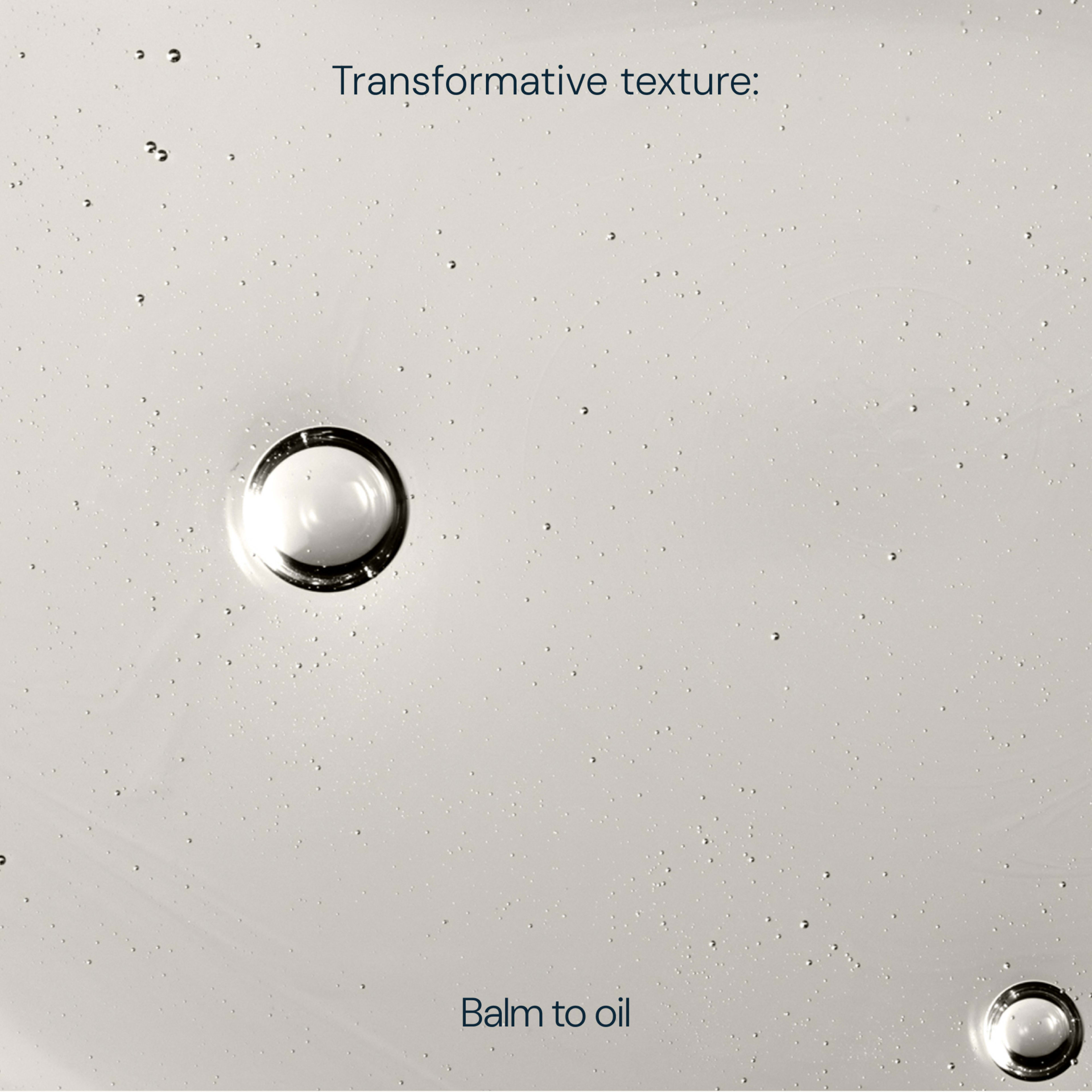 Close-up of clear liquid droplets on a pale surface with the text “Transformative texture: Balm to oil”, illustrating a skincare product that melts from balm into oil.