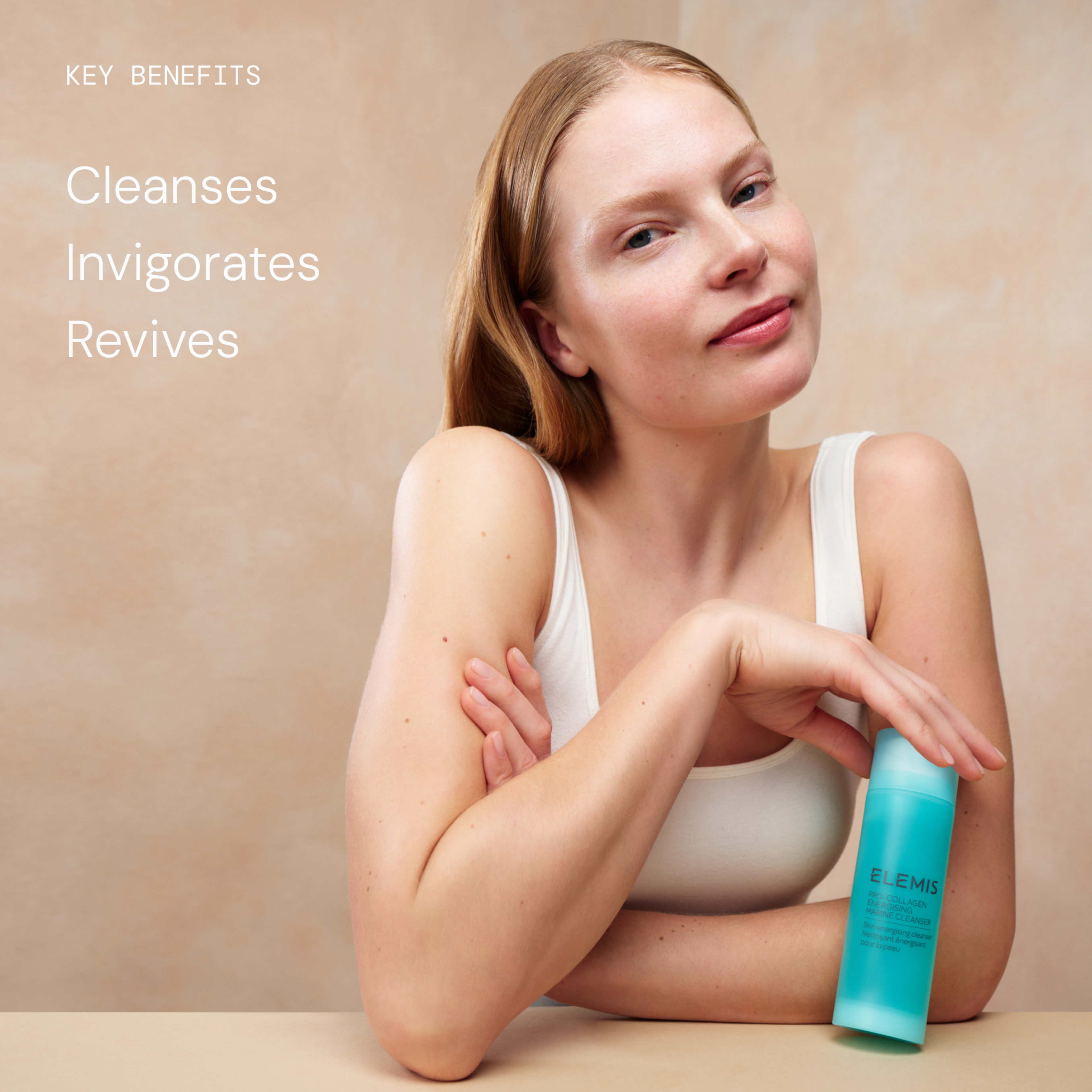 Woman in a white vest leaning on a table, lightly smiling and holding a turquoise ELEMIS Pro-Collagen cleanser bottle. On the left, text reads: “Key benefits – Cleanses, Invigorates, Revives.”