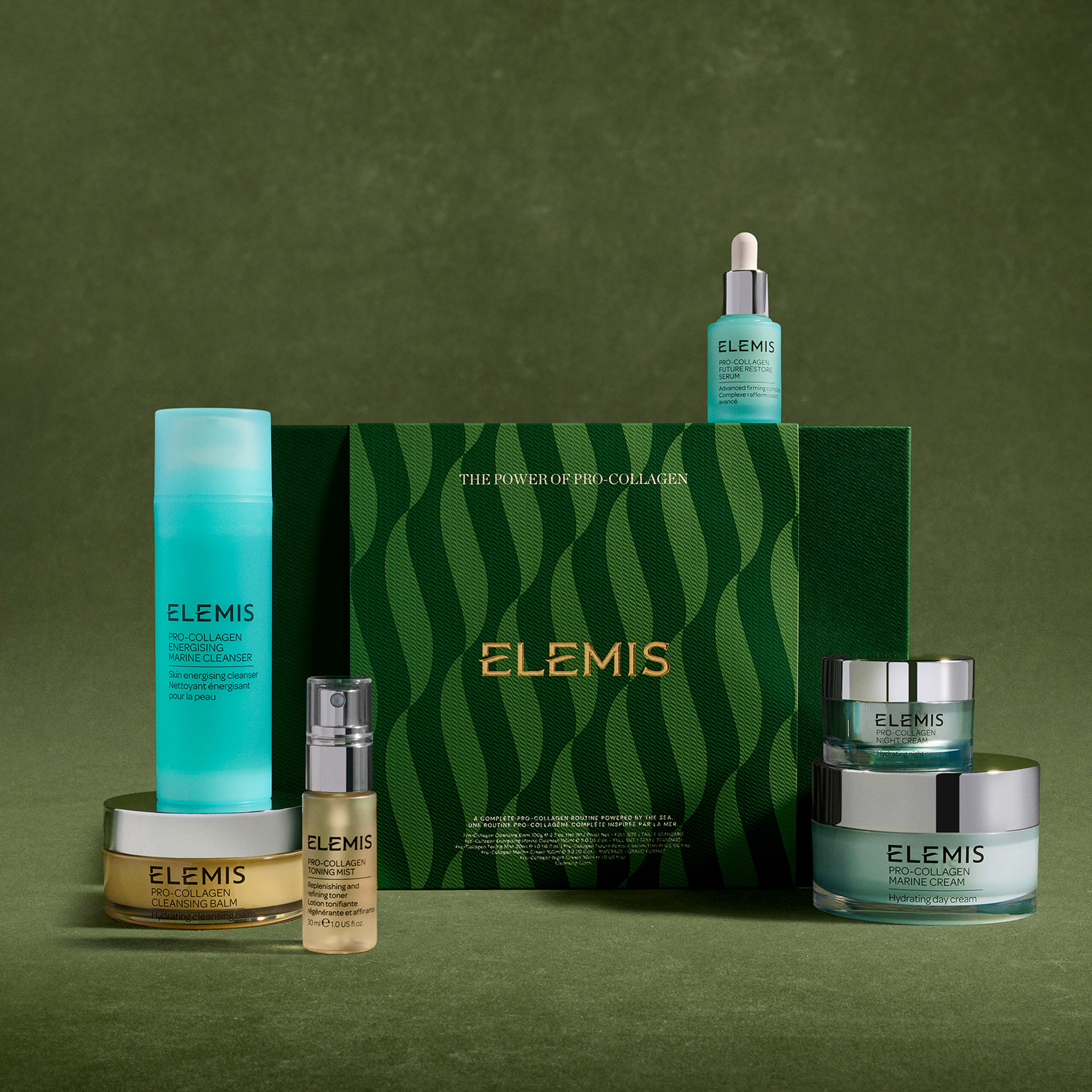 ELEMIS Pro-Collagen skincare gift set arranged against a green background, featuring a central green box reading "The Power of Pro-Collagen" and surrounding full-size products including cleanser, serums, eye cream and marine cream jars.