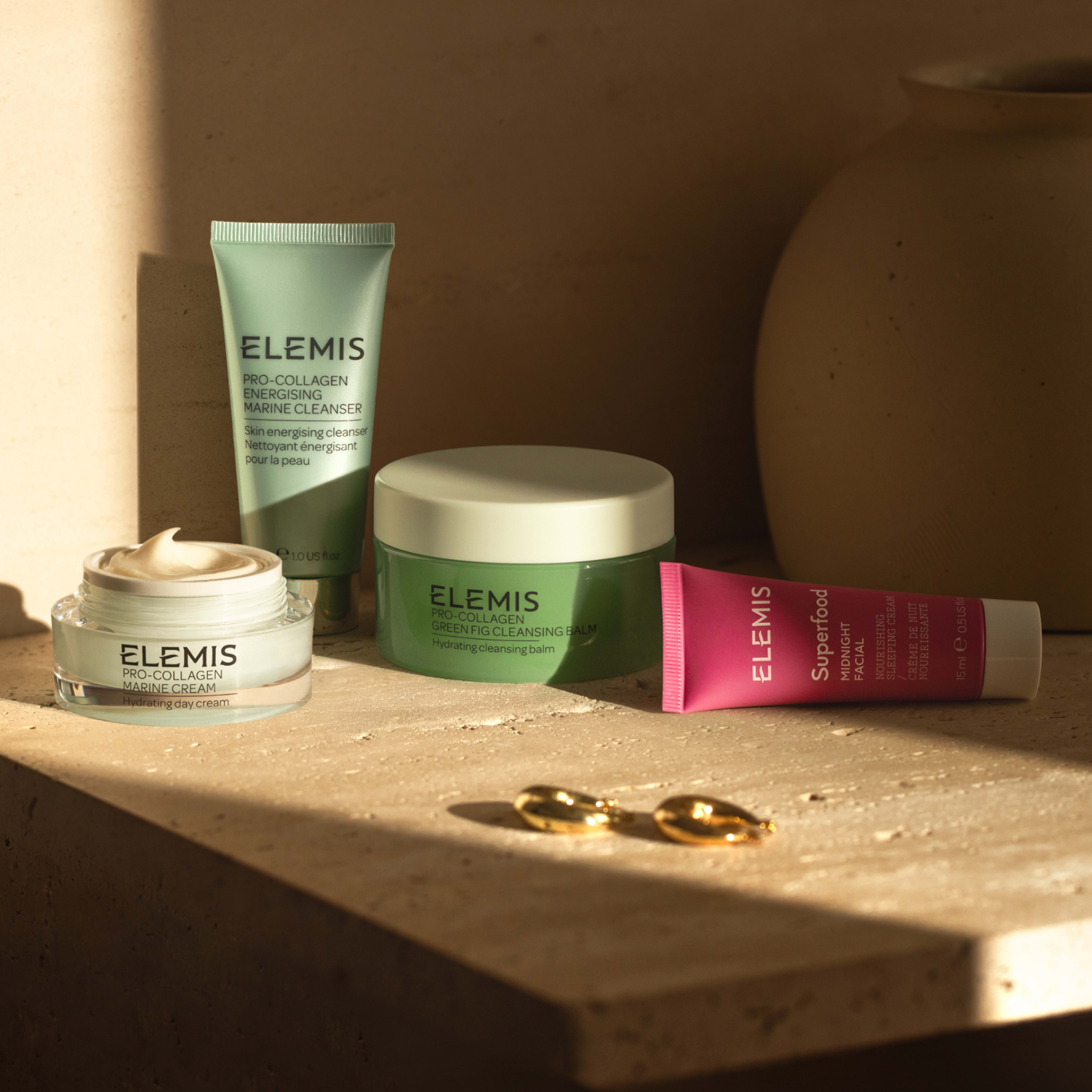ELEMIS skincare products, including Pro-Collagen Marine Cream, Pro-Collagen Energising Marine Cleanser, Pro-Collagen Cleansing Balm and Superfood cleanser, arranged on a sunlit stone surface beside a ceramic vase and two gold capsule supplements.