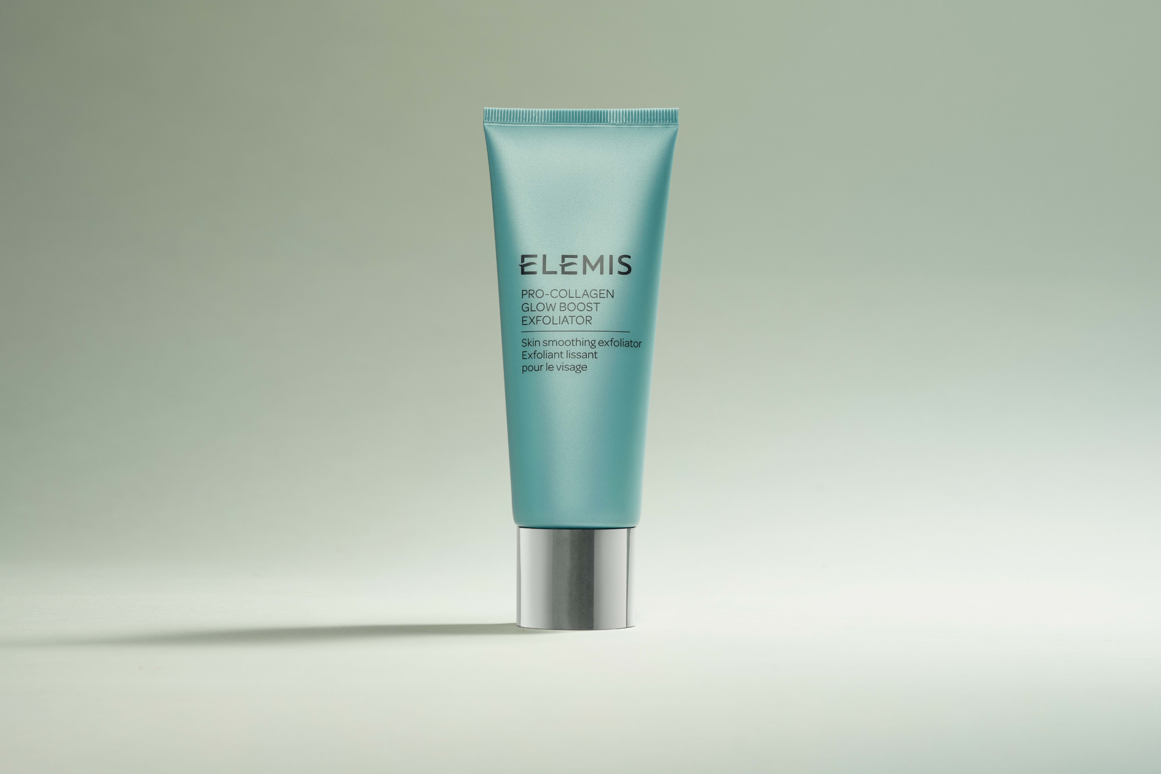 Multiple teal Elemis Pro-Collagen Glow Boost Exfoliator tubes with silver caps scattered on a light background.